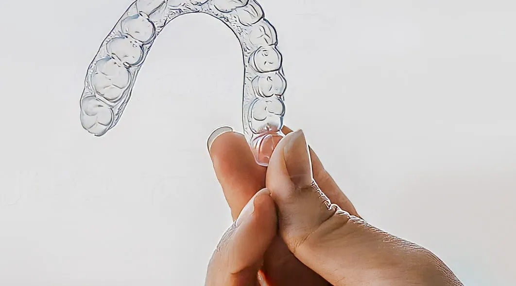 Uma mão segura uma placa transparente, moldada aos dentes.