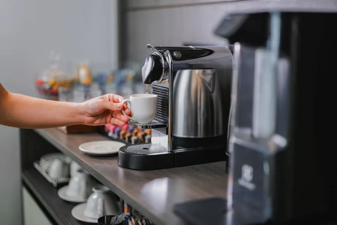 Mão retirando uma xícara de café da máquina, na estação de café do consultório
