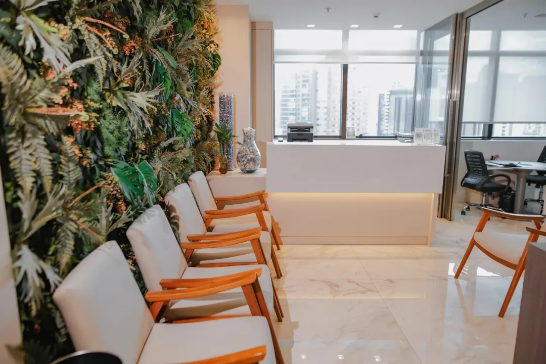 Sala de espera do consultório, com poltronas alinhadas diante da parede de plantas e o balcão da recepção ao fundo