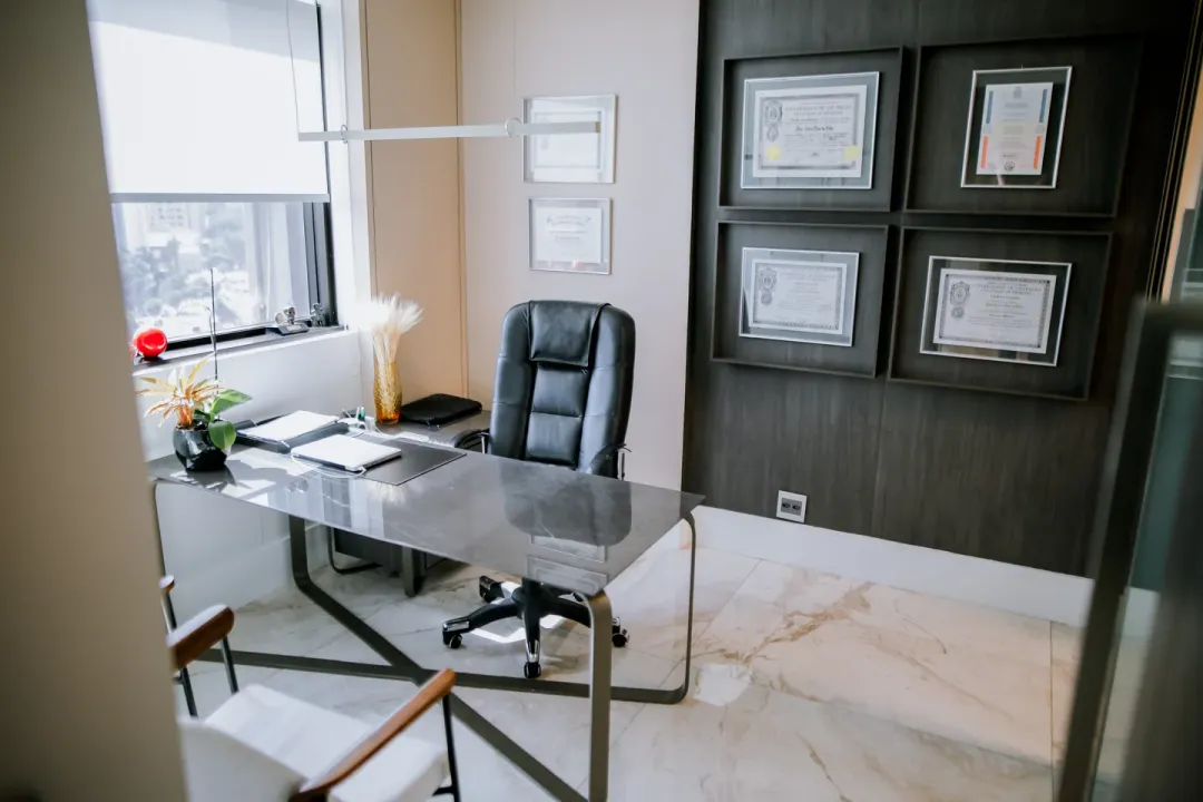 Sala de consulta do Dr. José Carlos Faes, com mesa de vidro e diplomas emoldurados na parede